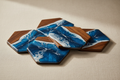 High-end studio product shot of a set of 4 hexagonal coasters with blue and white swirl resin inlay arranged artistically on a clean beige background. Detailed macro view of the texture. Soft studio lighting, sharp focus, minimal shadows, luxury catalog style, 8K.